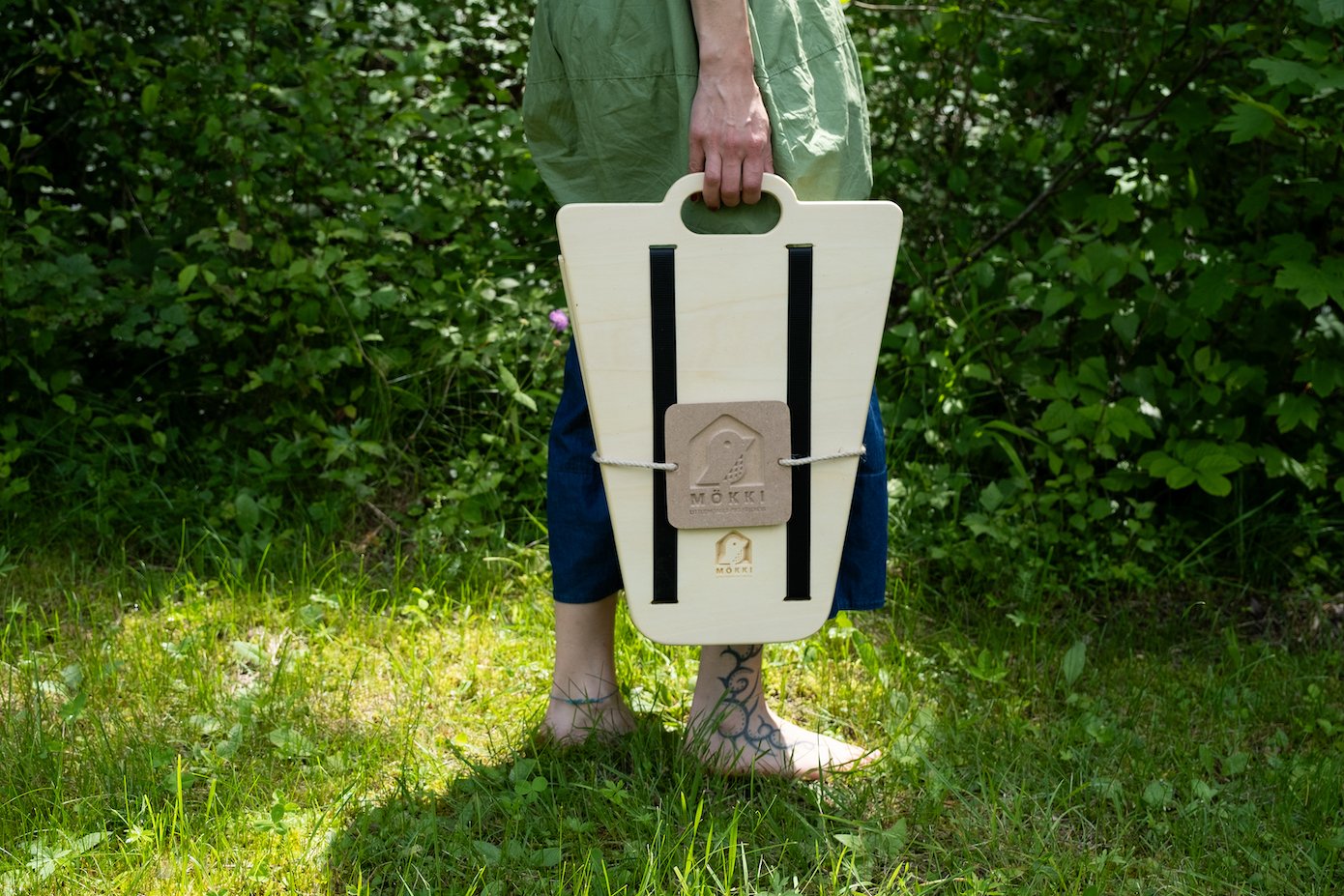 Closed view of the Made in Italy bird feeder from the MÖKKI collection by Ulap design. A woman barefoot on the lawn holds the closed manger in her hand.