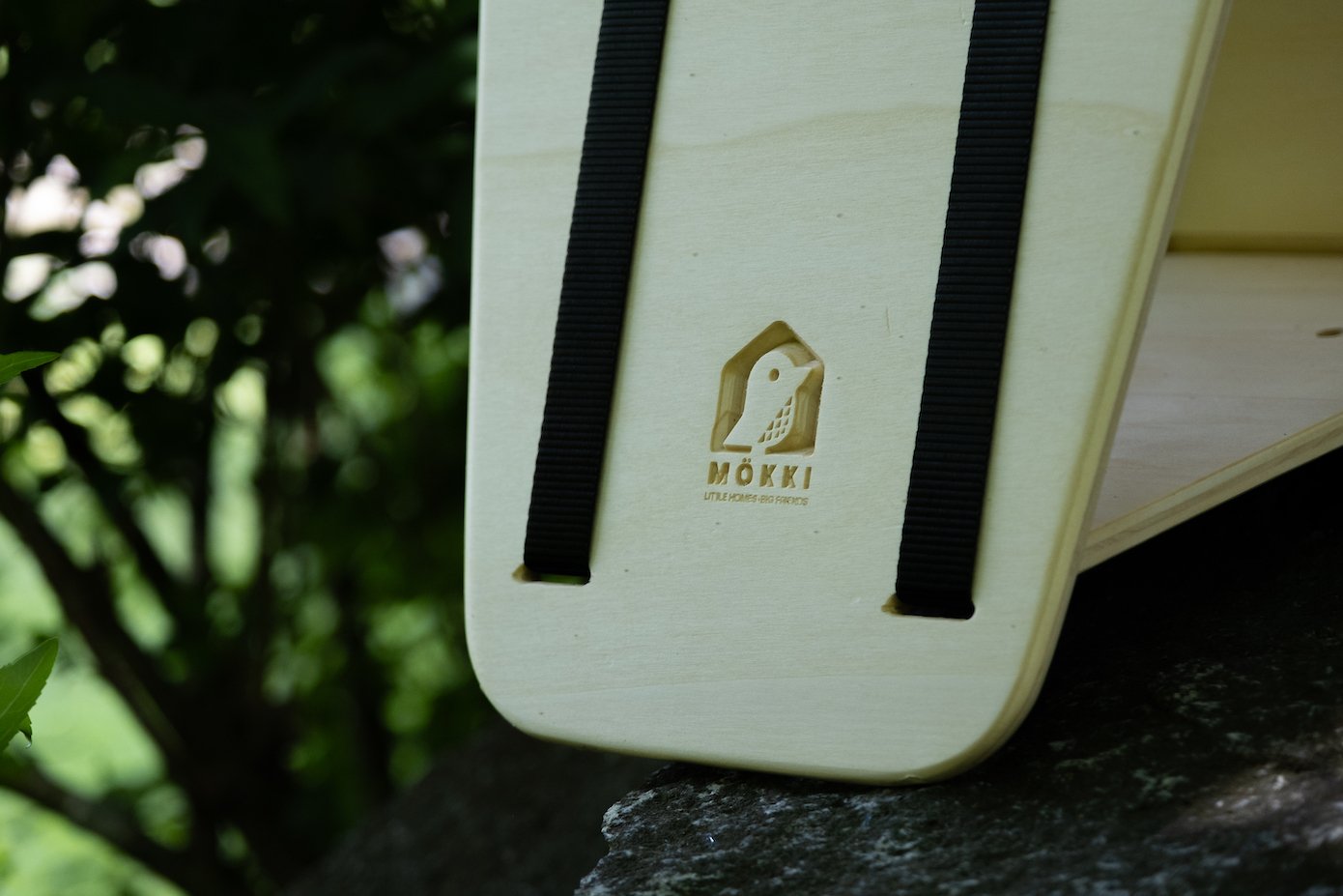 Detail view of a MÖKKI bird feeder by Ulap design made of birch wood and black straps.