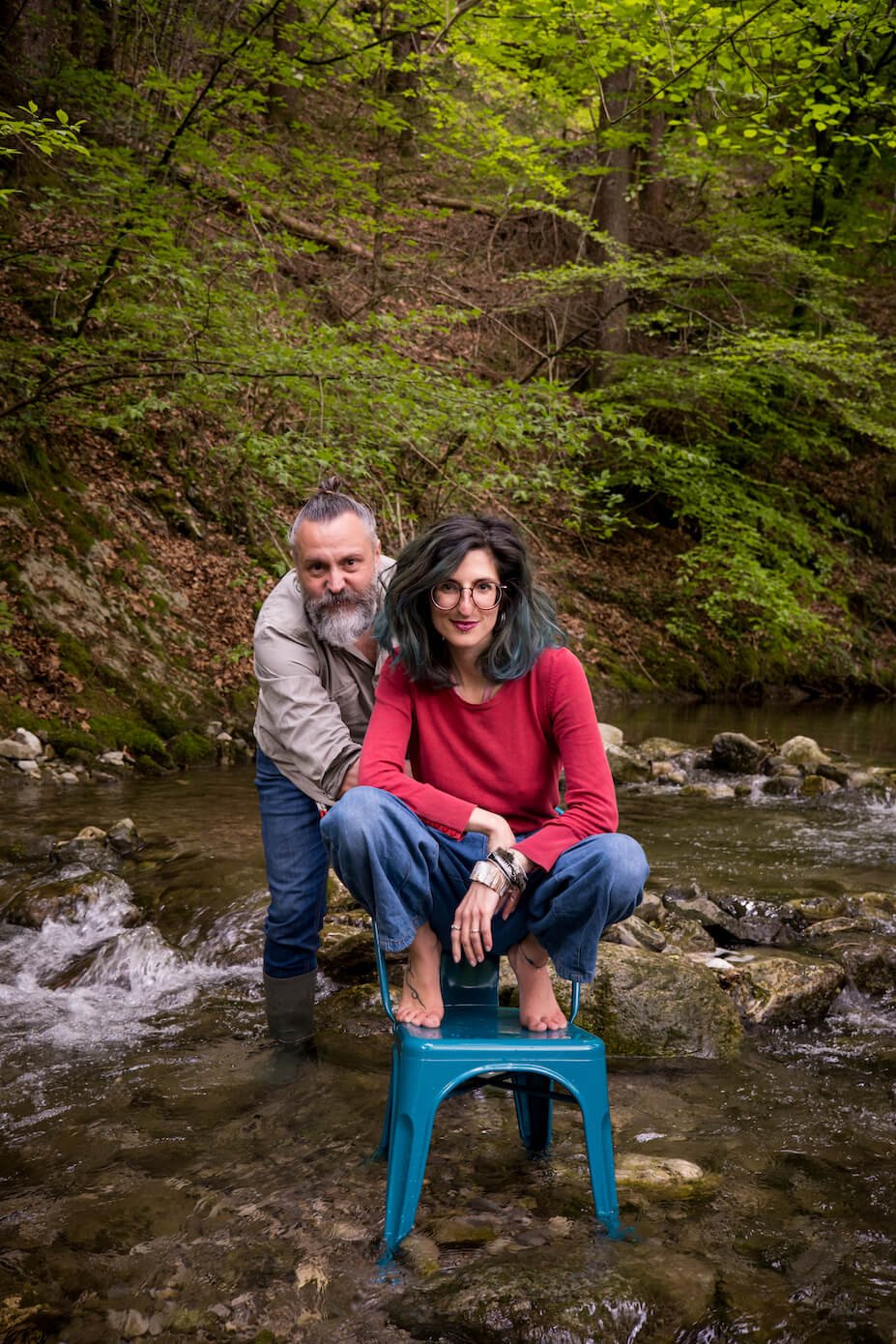 Photography by Cris Tumedei and Andrea Pregl: the Ulap design team that created the project for the protection of biodiversity and the Made in Italy products of the MÖKKI collection. The two find themselves in the middle of a mountain stream, surrounded by woods. She is crouched in a petrol-colored designer chair, he standing behind her.